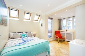 A bedroom with a bed, a red chair, a radiator, and a window. - Magic Properties (London)