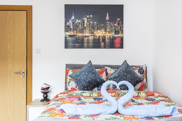 A hotel room with a bed featuring a floral bedspread, two decorative pillows, a globe on a bedside table, and a cityscape painting above the bed. - Magic Properties (London)