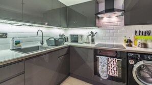 Una cucina moderna con mobili scuri, forno integrato, lavastoviglie e un piano di lavoro con diversi utensili da cucina.