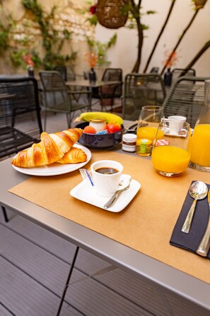 A breakfast table with croissants, coffee, juice, and a fruit bowl.