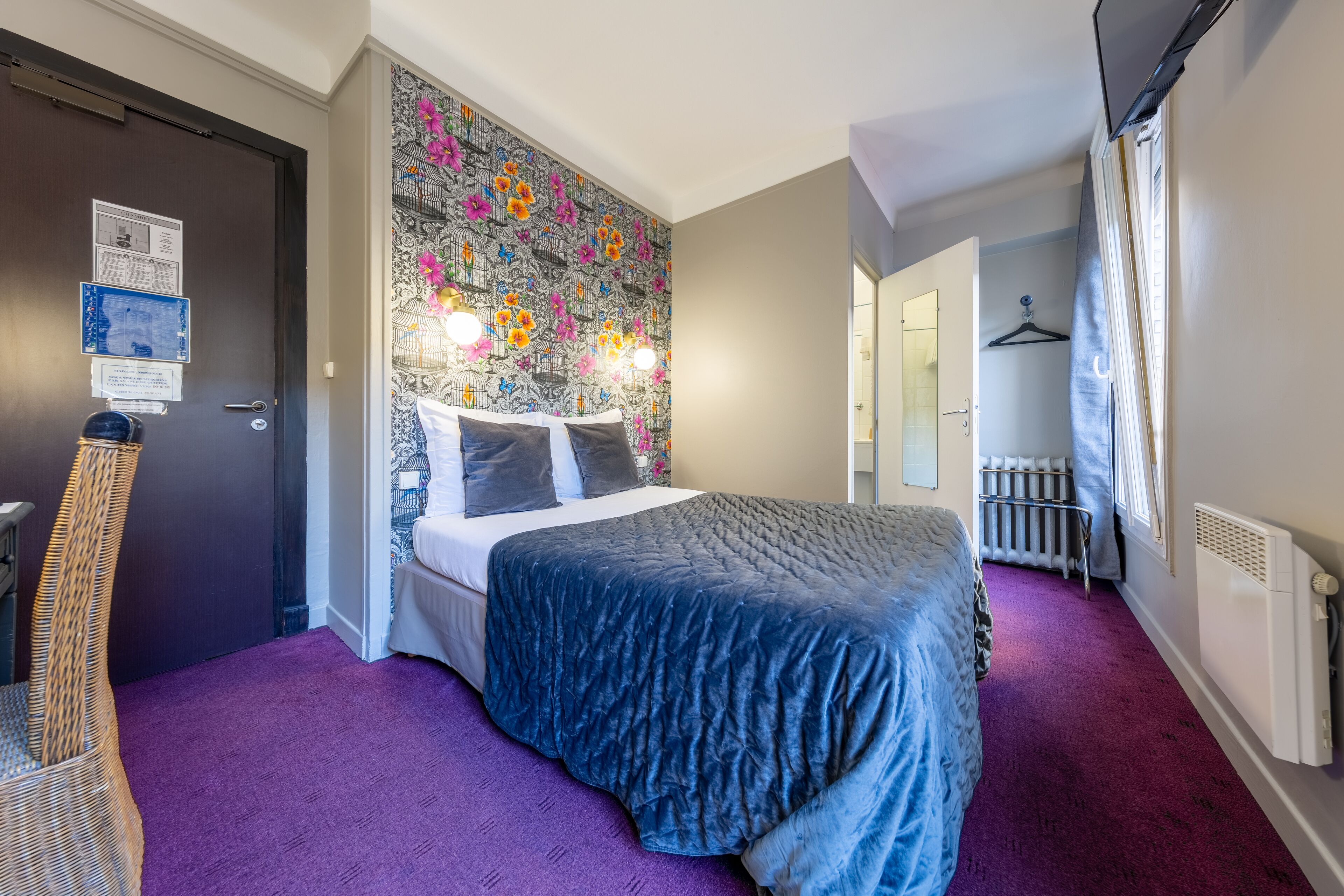 Un dormitorio con una cama grande, un cabecero floral de colores, una alfombra morada y un radiador.