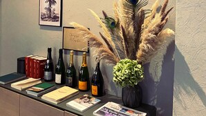 A reception area with a counter displaying wine bottles, books, and a framed picture of a palm tree. - Hôtel Azur Reims (Reims)