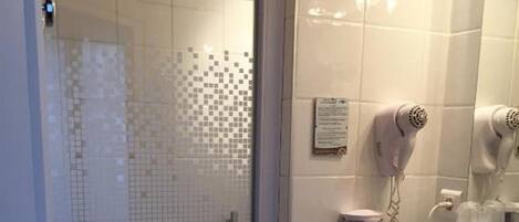 A bathroom with a glass shower enclosure, a white sink, and a hairdryer mounted on the wall.
