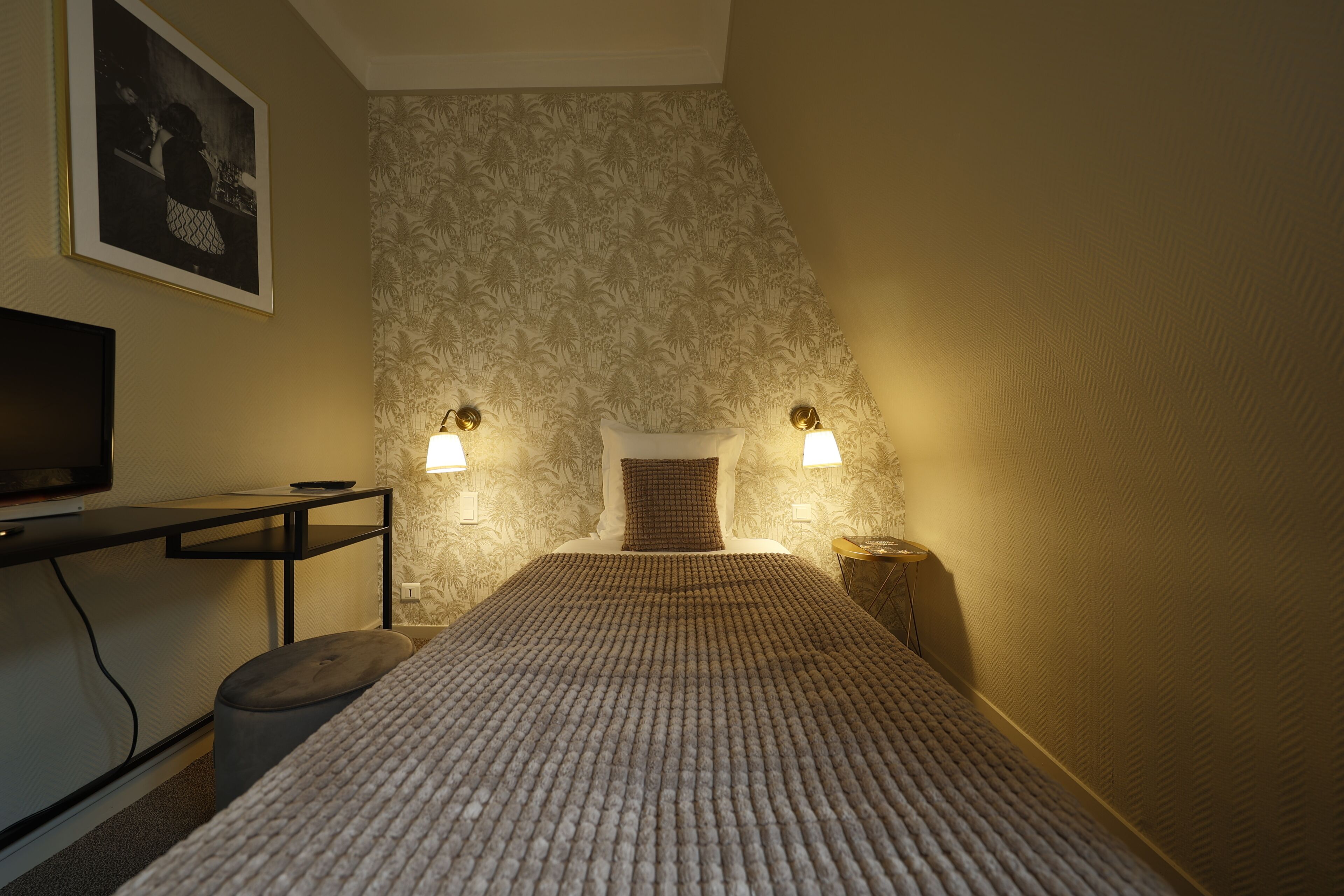 A bedroom with a bed, a desk, a chair, a television, and two wall-mounted lamps.