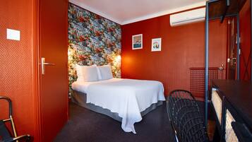 Habitación de hotel con cama, escritorio, silla y pared con un mural colorido.