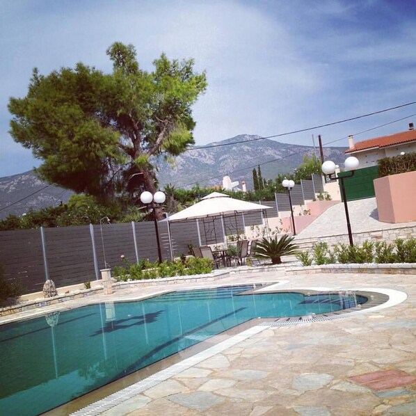 A swimming pool with a stone deck, surrounded by a fence, with a mountain in the background.