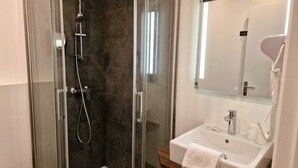 Un baño moderno con ducha de vidrio, un lavamanos blanco y un espejo sobre él.