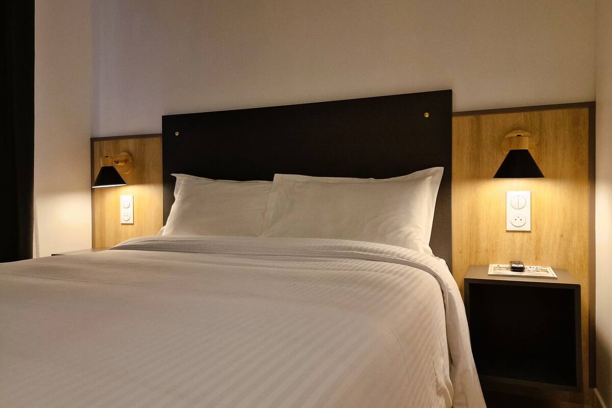 A neatly made bed with a headboard, two bedside tables with lamps, and a wall socket.