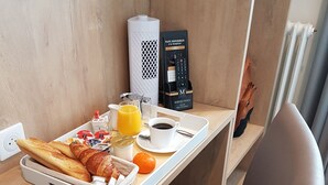 Una bandeja de desayuno con cruasanes, jugo de naranja, café y un muffin sobre una mesa de madera.