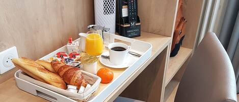 A breakfast tray with croissants, orange juice, coffee, and a muffin on a wooden table.