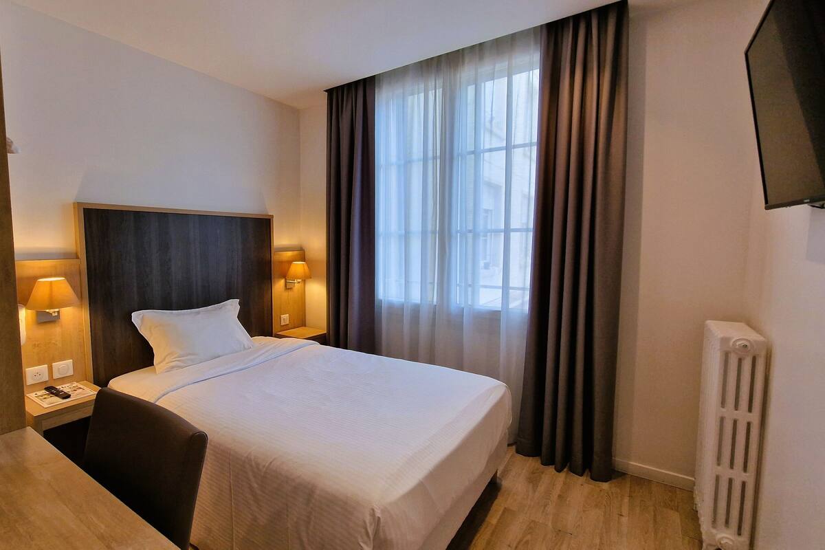A hotel room with a bed, bedside lamps, a desk, and a TV mounted on the wall.