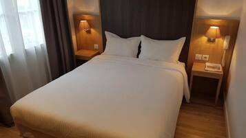 A hotel room with a large bed, two bedside tables, a nightstand, a lamp, and a telephone.