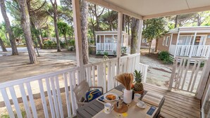 A covered outdoor seating area with a table set for breakfast, surrounded by trees and mobile homes. - Club Del Sole Viareggio Family Collection (Viareggio)
