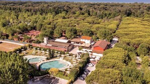 An aerial view of a resort with multiple swimming pools, a parking area, and a dense forest surrounding the property.