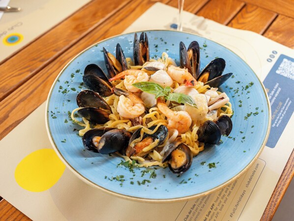 Un plato de pasta con mariscos sobre una mesa de madera, con un menú desenfocado al fondo.