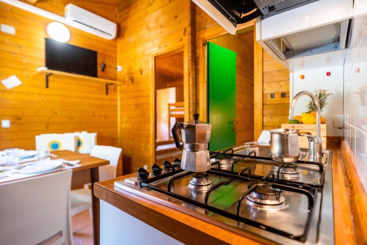 A wooden interior with a kitchen area featuring a stove, a coffee maker, and a green screen.