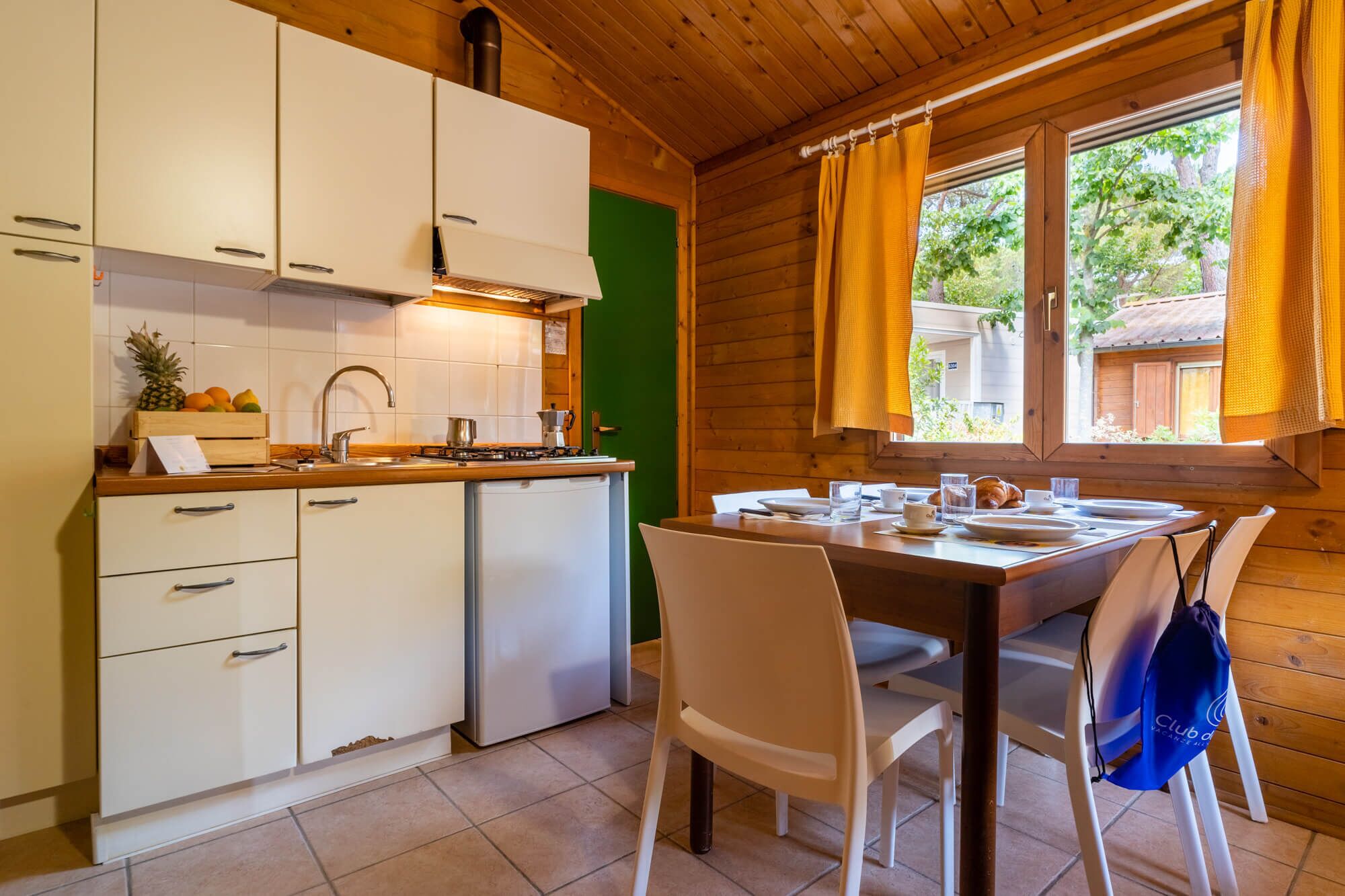 Una cocina compacta con armarios blancos, un refrigerador pequeño y un comedor con una mesa dispuesta para dos.