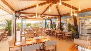 An outdoor restaurant with wooden tables and chairs, hanging light bulbs, and a view of the surrounding landscape.