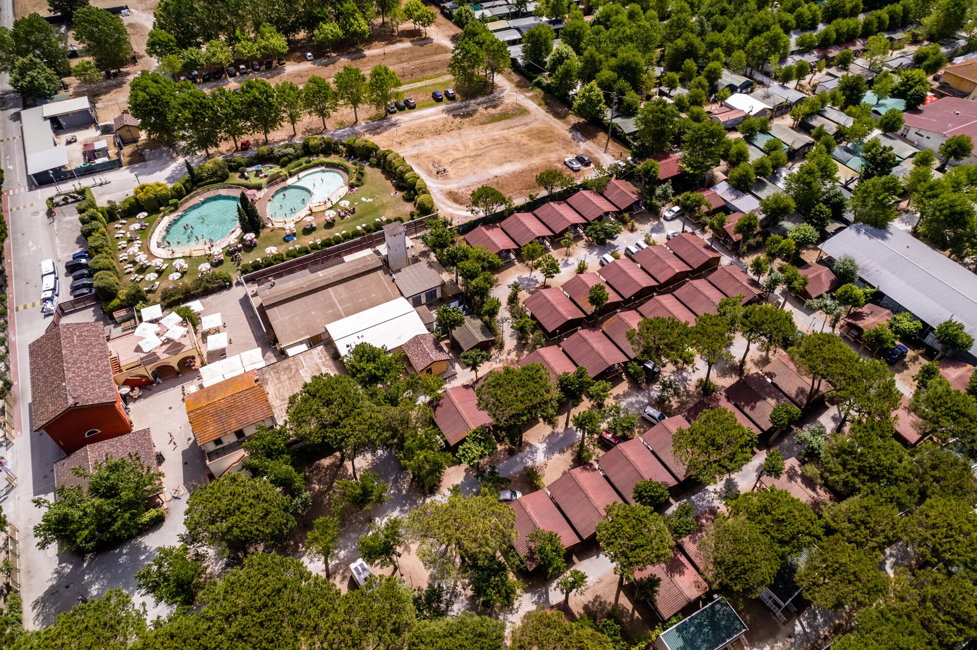 Vista aérea de um resort com várias piscinas, uma ampla área aberta e um conjunto denso de edifícios com telhados vermelhos.