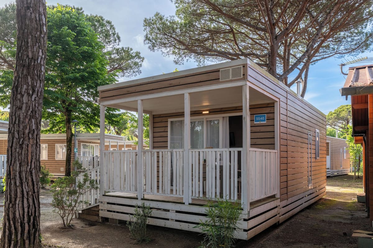 A small wooden cabin with a porch, a number sign, and a view of other cabins.