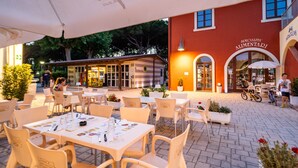 An outdoor dining area with tables and chairs, a building with a red facade, and a bicycle parked outside.