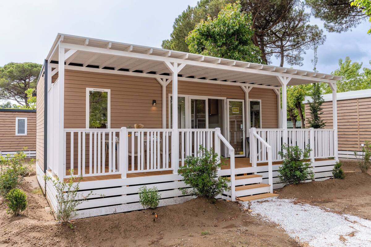 A mobile home with a covered porch, a door, and a small garden area.