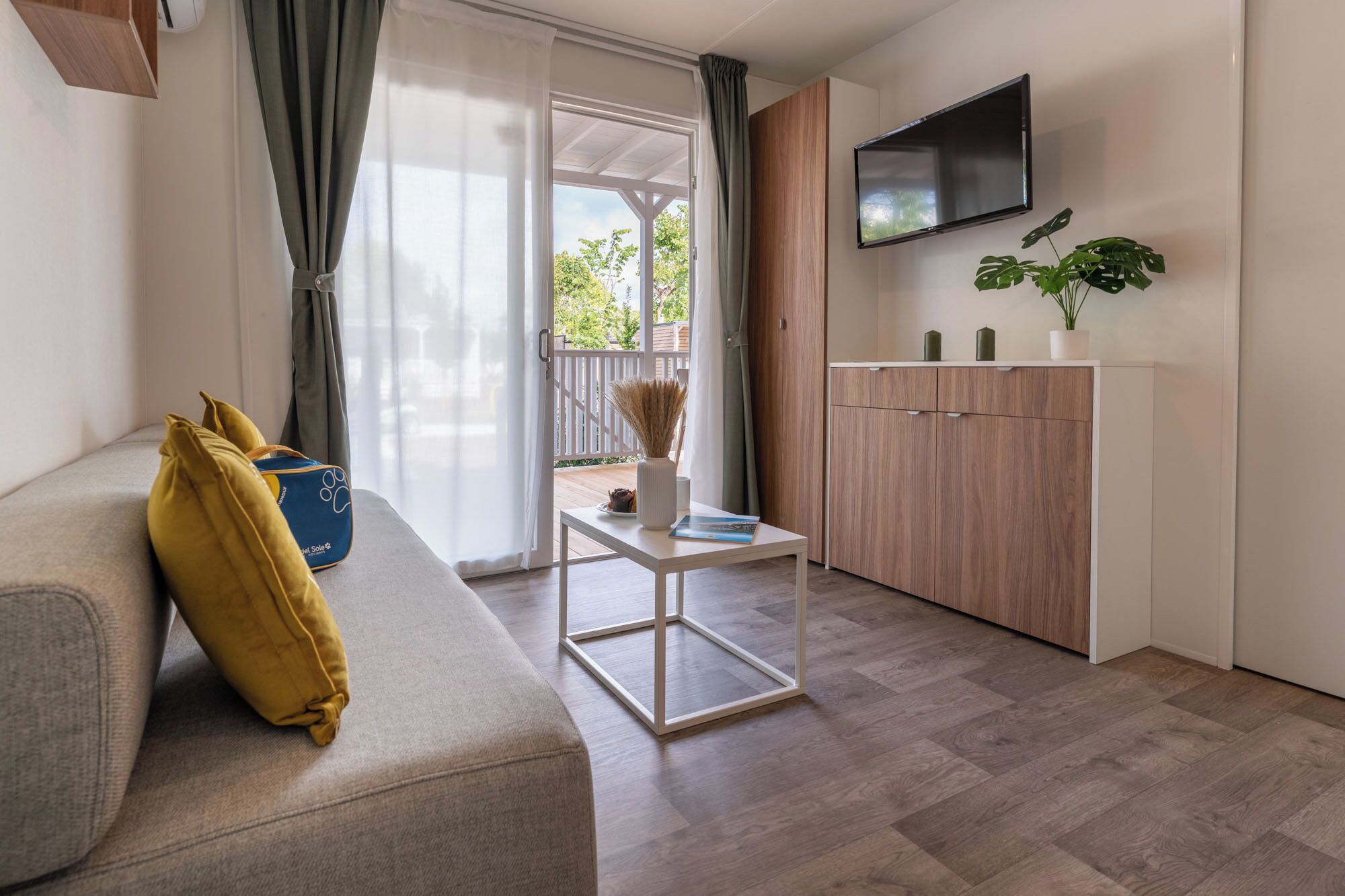 A modern living room with a sofa, a small table, a TV mounted on the wall, and a wooden cabinet.
