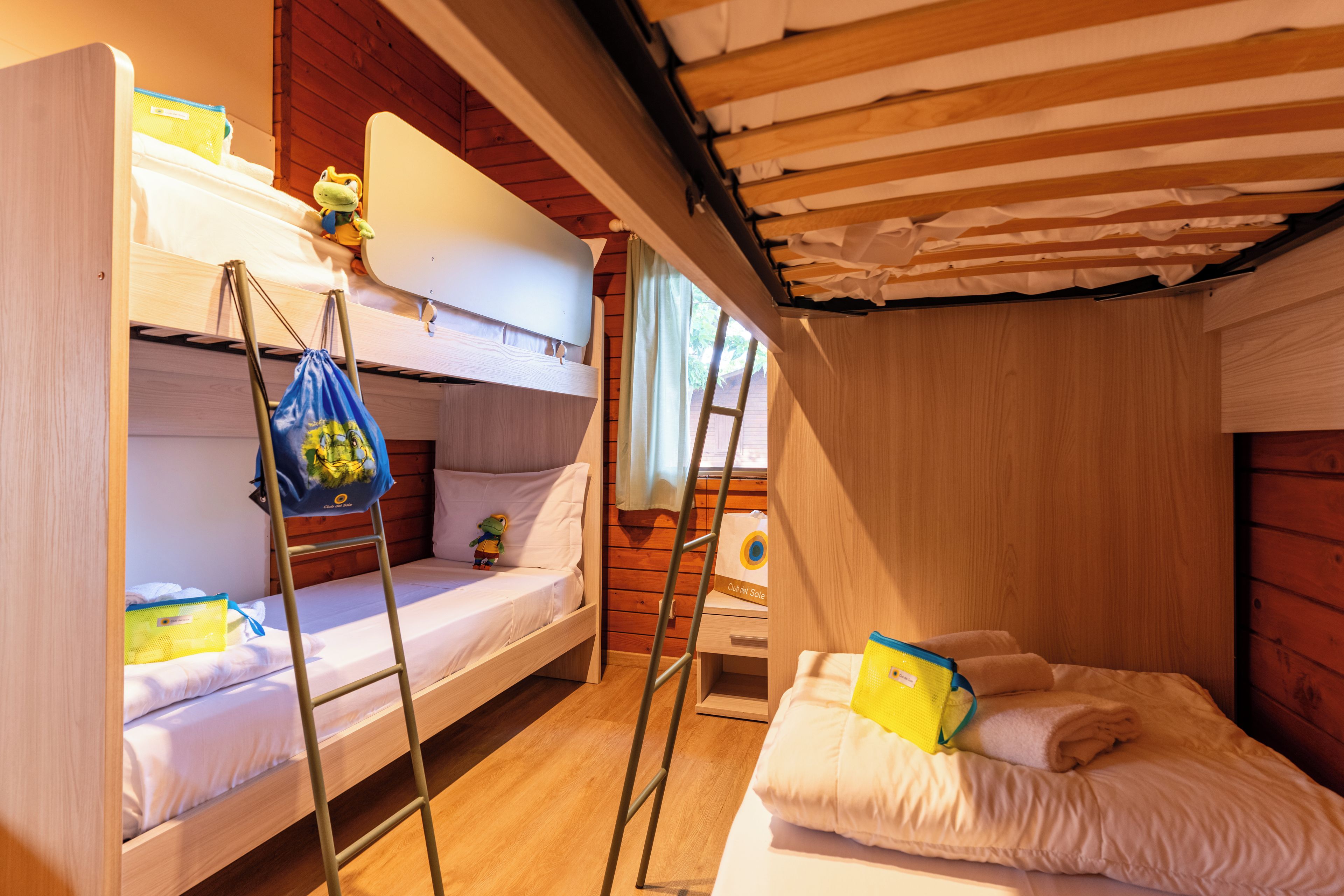 A bunk bed room with a ladder, a small table, and a window with curtains.