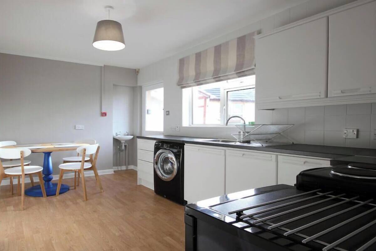 A compact kitchen with a washing machine, a sink, and a dining area with chairs.