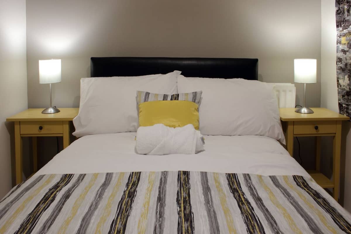 A neatly made bed with a striped bedspread, two bedside lamps, and a black headboard.