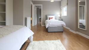 A bedroom with a large bed, a smaller bed, a grey bench, a white rug, and a walk-in closet. - KC Accommodation (Dungannon)
