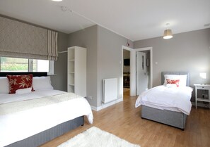 A bedroom with two beds, a walk-in closet, a radiator, and a view of the garden. - KC Accommodation (Dungannon)