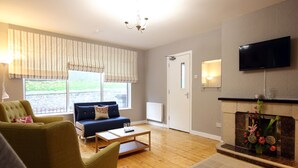 A living room with a sofa, armchairs, a coffee table, a fireplace, and a TV mounted on the wall. - KC Accommodation (Dungannon)