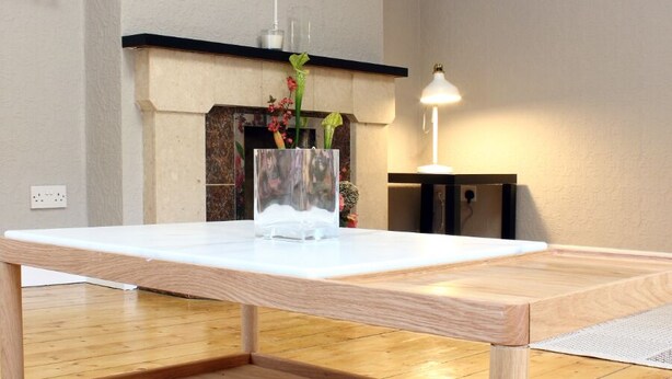 A modern living room with a wooden coffee table, a flat-screen TV mounted on the wall, and a fireplace with a vase of flowers. - KC Accommodation (Dungannon)