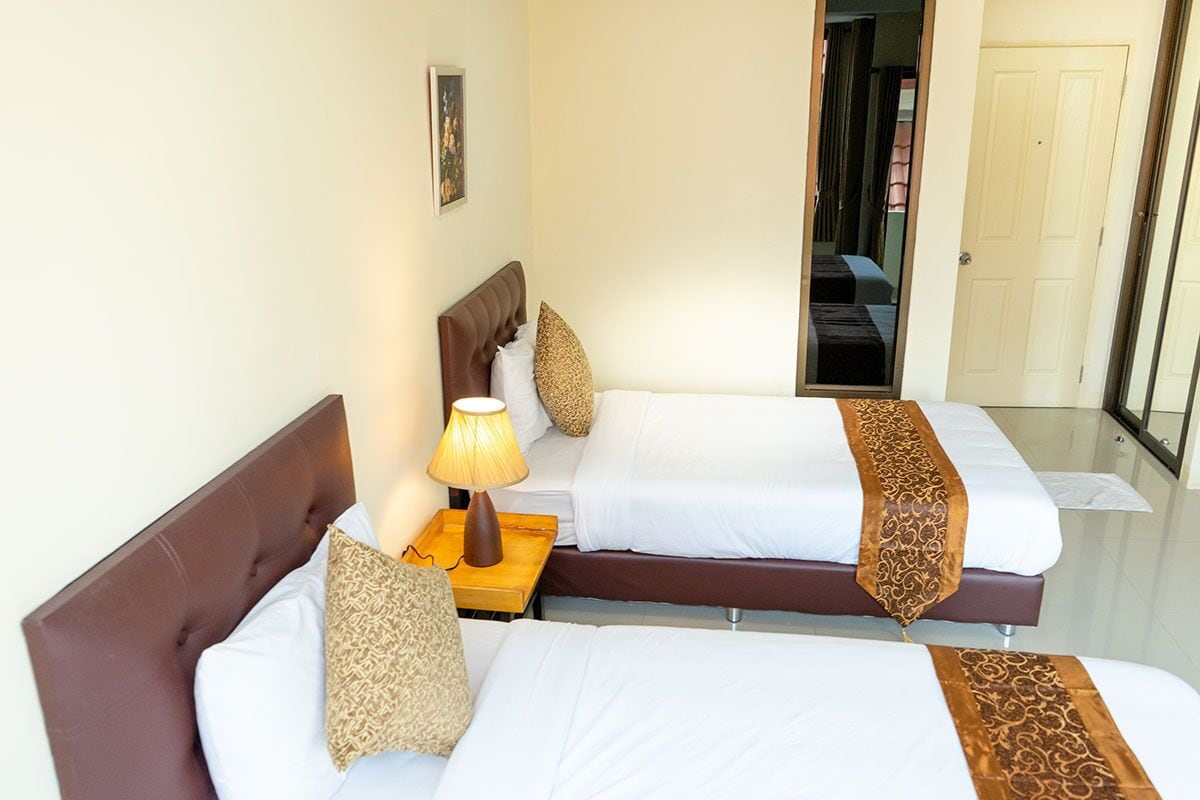 Une chambre d’hôtel avec deux lits, une table de chevet avec une lampe et une porte donnant sur une autre pièce.