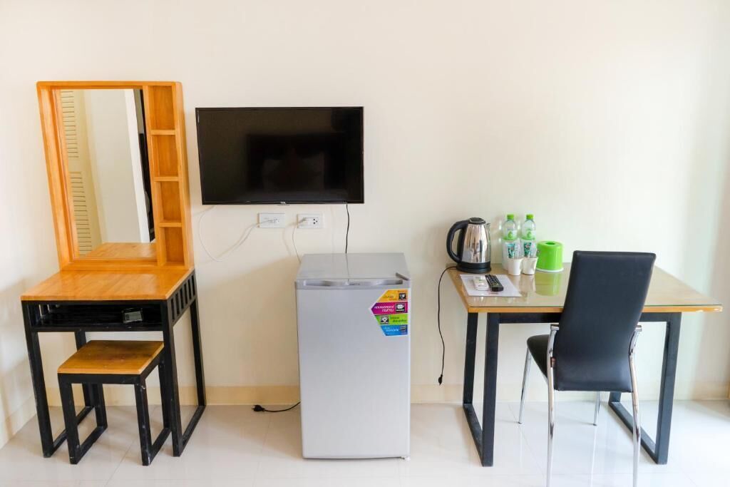 Een kleine kamer met een houten bureau, een zwarte stoel, een witte koelkast, een televisie en een spiegel.
