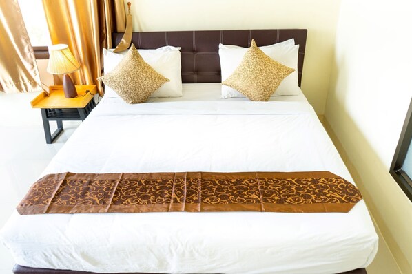A neatly made bed with a patterned bedspread, two pillows with intricate designs, and a bedside table with a lamp. - Sasi Nonthaburi Hotel (Bang Bua Thong)