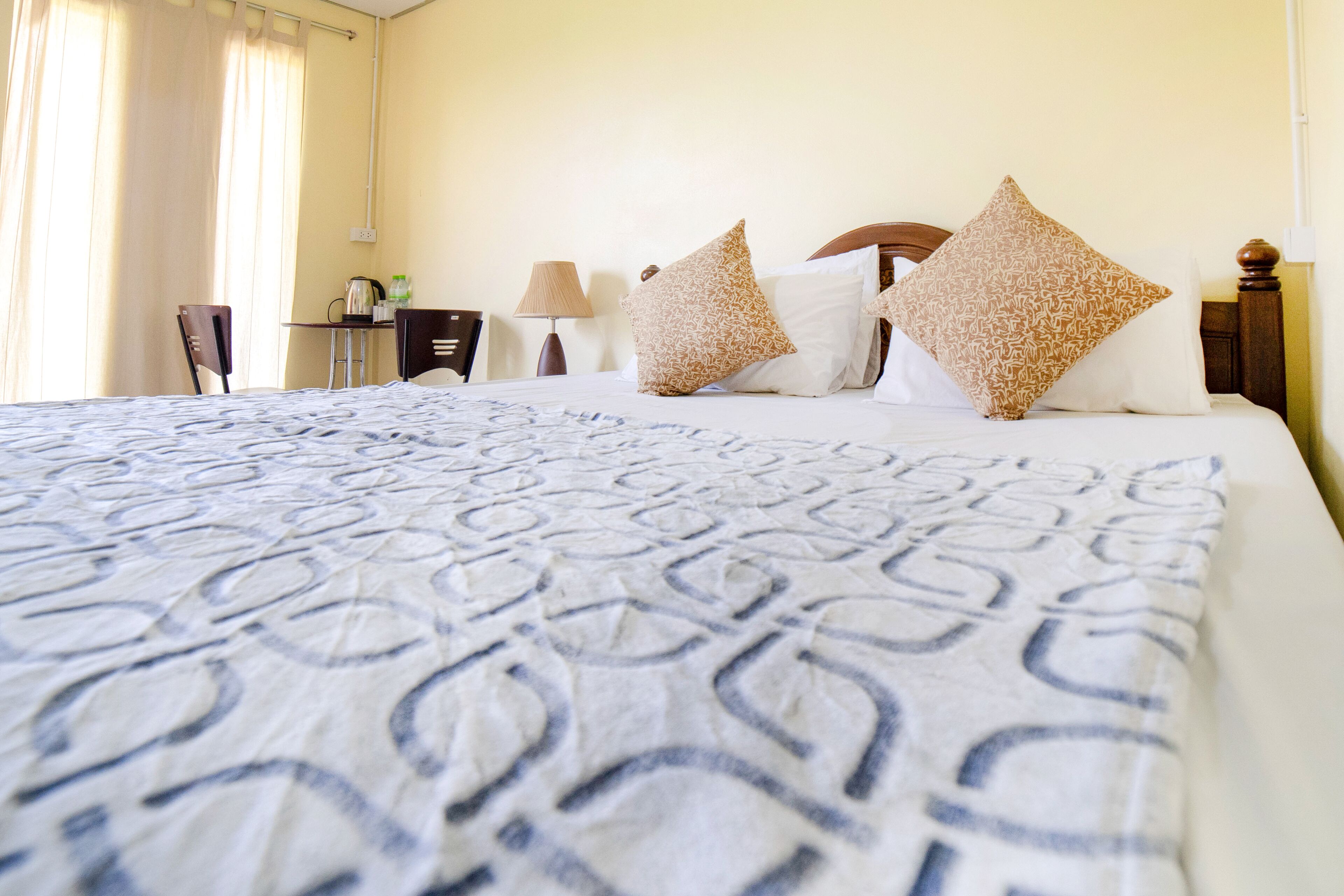 A hotel room with a large bed, two pillows, a desk with a lamp, and a chair.