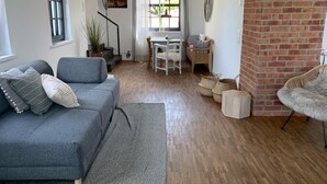 Una sala de estar acogedora con un sofá gris, una mesa de comedor con sillas, un pequeño banco de madera y una chimenea de ladrillo.