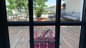 Una terraza de madera con mobiliario exterior, una planta en maceta y una cesta de mimbre con botellas.