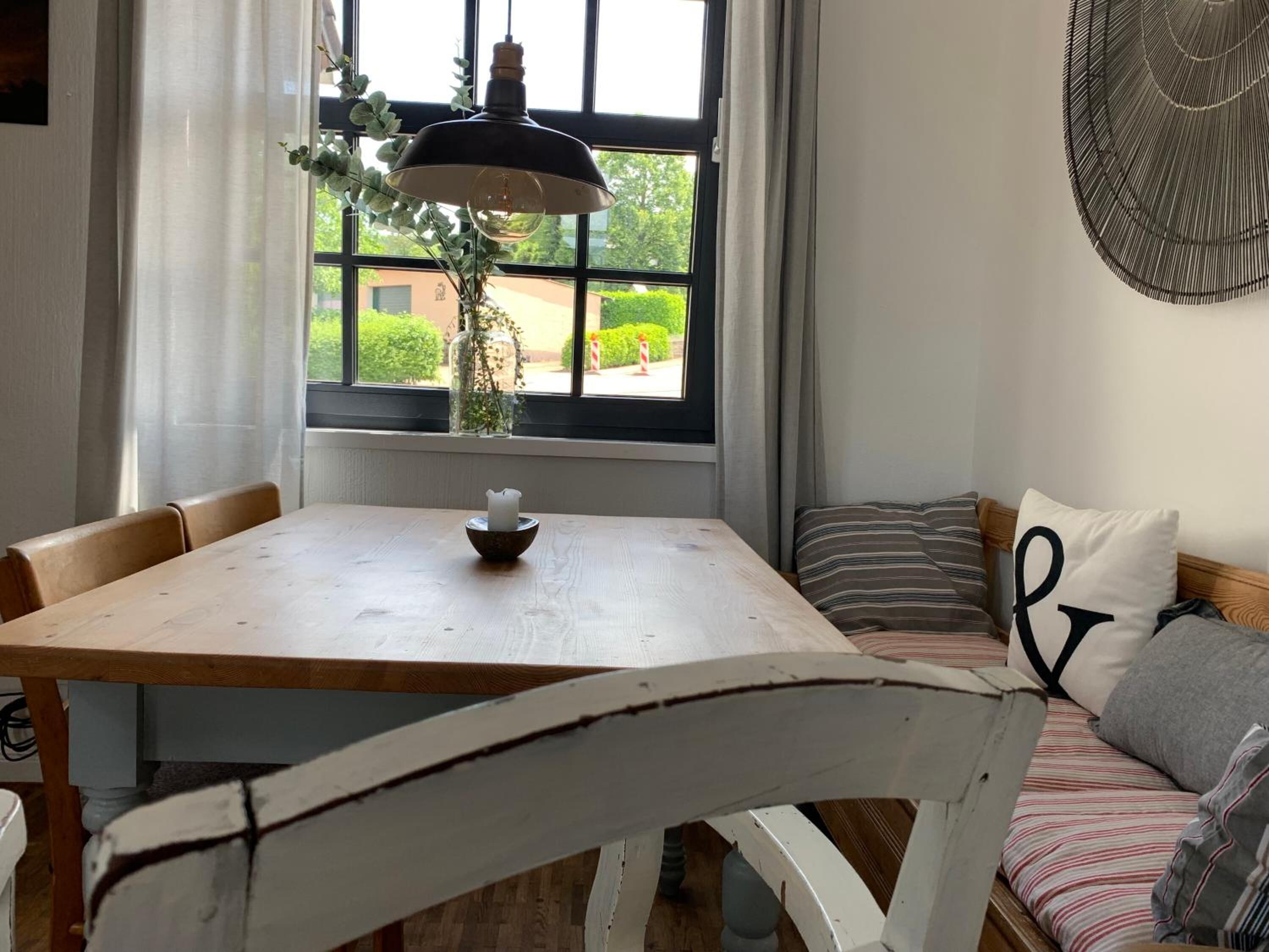 A cozy dining area with a wooden table, a bench with cushions, and a hanging light fixture.