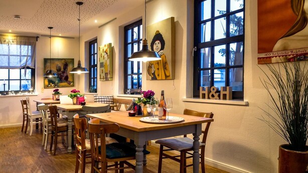 Un comedor con mesas y sillas de madera, ventanas amplias y obras de arte en las paredes.
