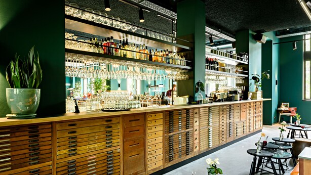 A bar area with shelves of bottles and glasses, wooden cabinets, and seating areas. - Conscious Hotel Westerpark (Amsterdam)
