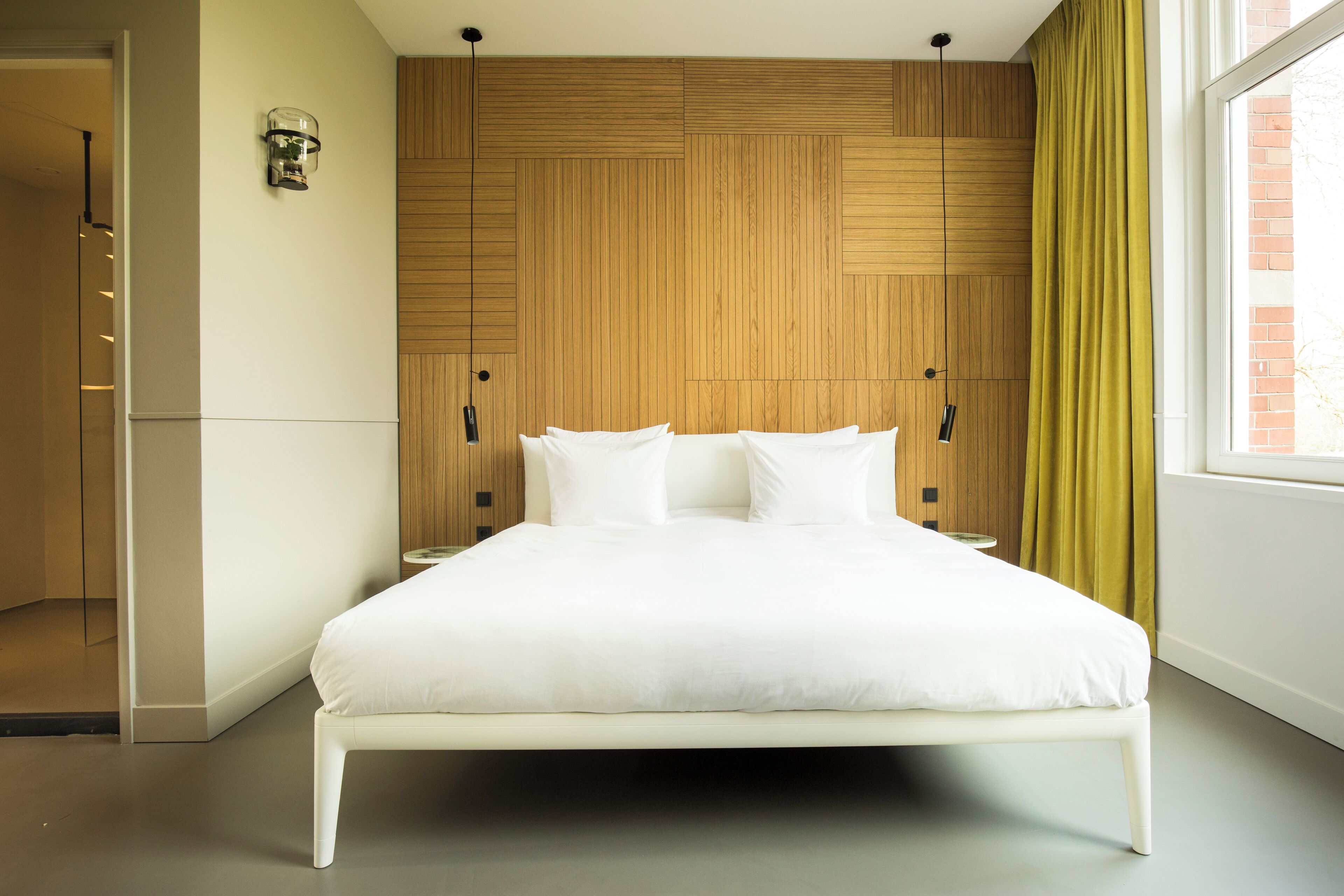 Een moderne slaapkamer met een houten hoofdbord, een groot bed met witte lakens, een nachtkastje en een raam met gordijnen.