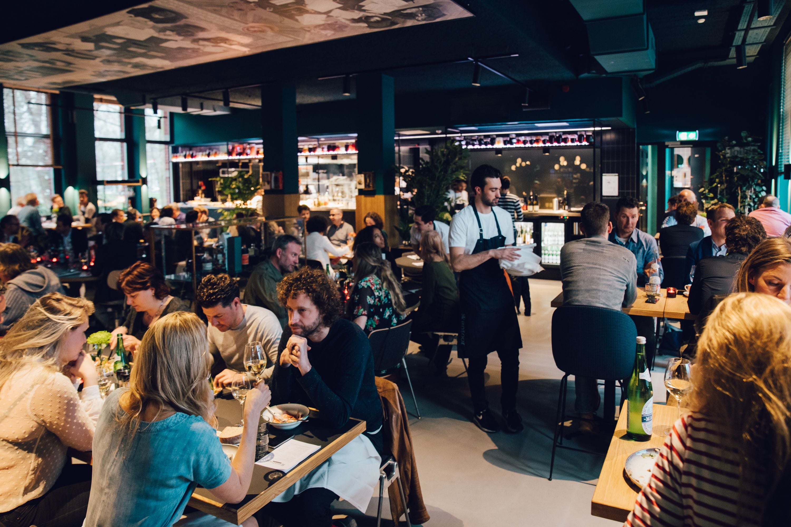 A busy restaurant with patrons dining and a waiter attending to them.