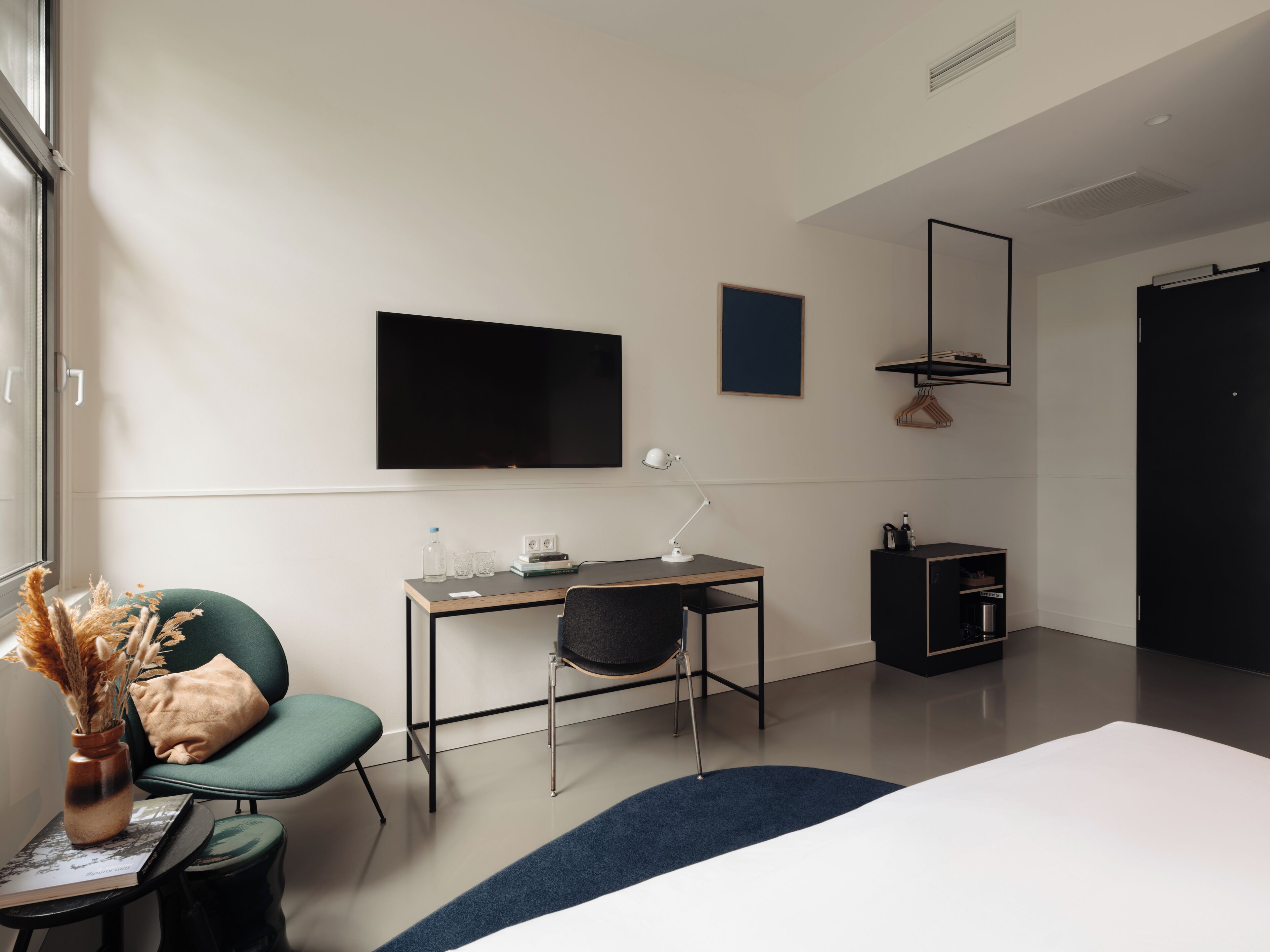 A modern hotel room with a bed, a desk with a chair, a TV, and a wardrobe.