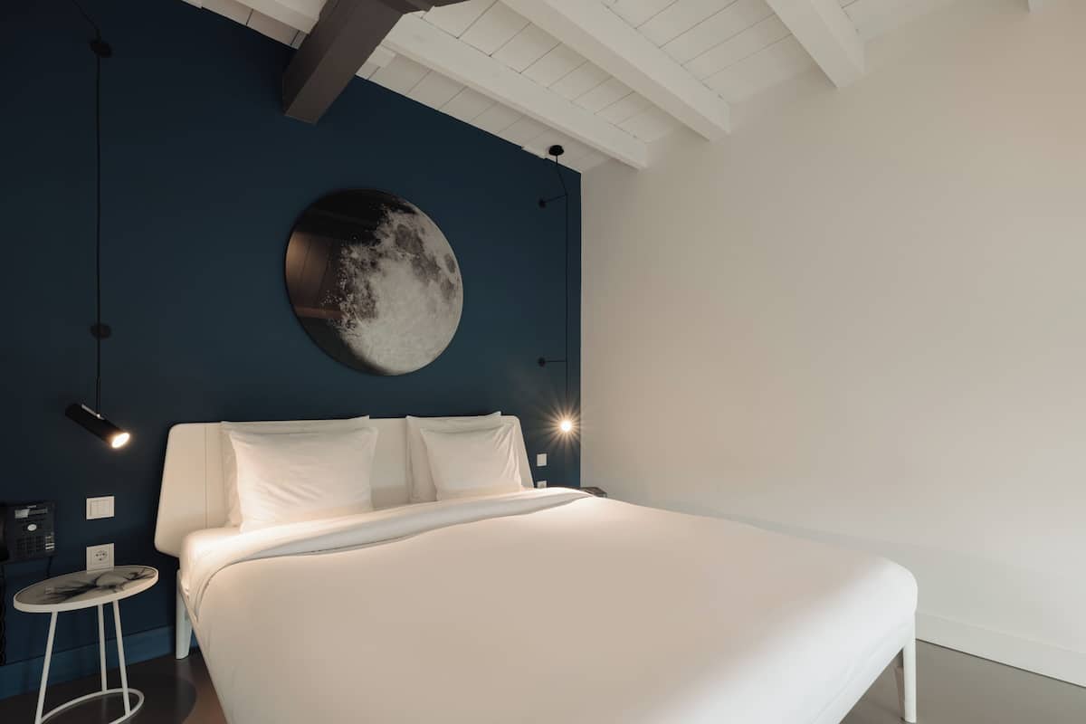 Un dormitorio moderno con una cama grande, un reloj de pared redondo y una mesita de noche pequeña.