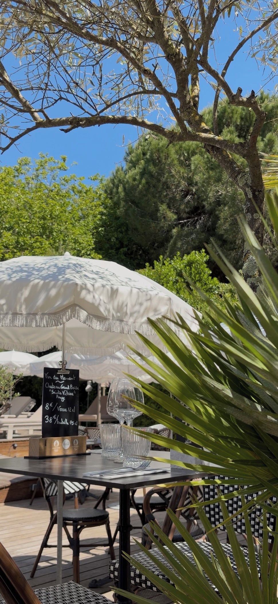 An outdoor dining area with a table and chairs, a white umbrella, and a menu stand.