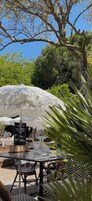 Un área de comedor al aire libre con una mesa, sillas, un paraguas blanco y un atril para el menú.