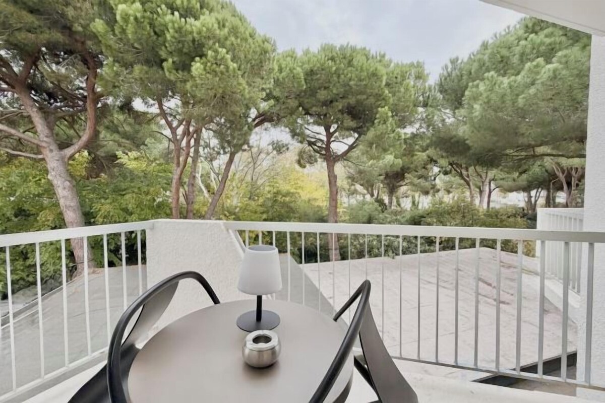 A balcony with a table and chairs, overlooking a garden with trees.